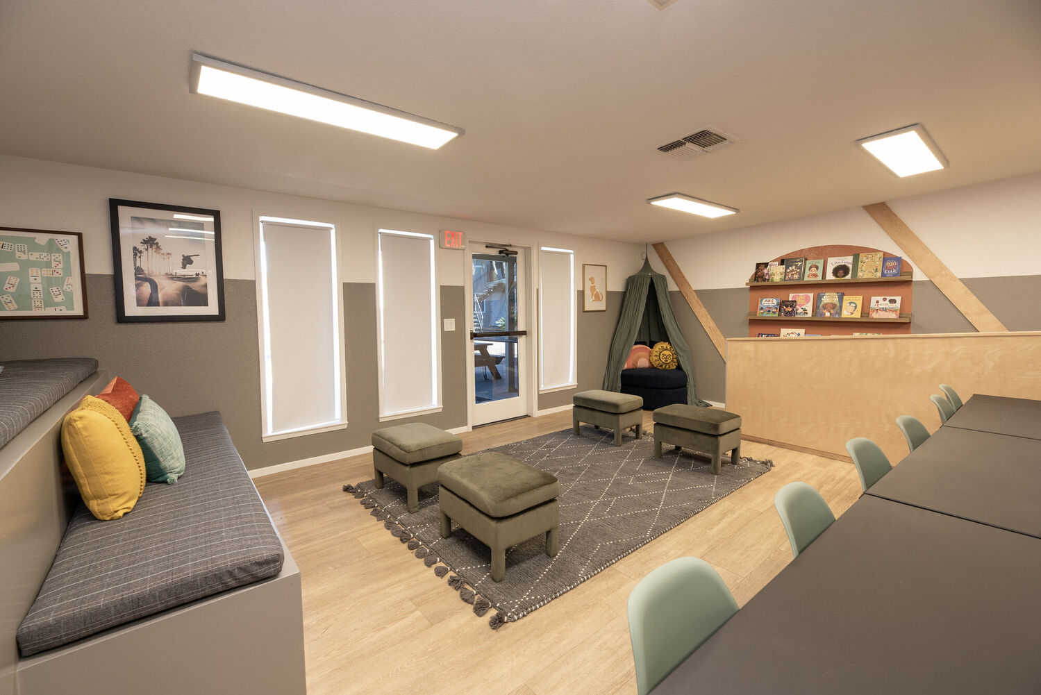 Reading area with cushions and kids books on a shelf as well as a long table with chairs